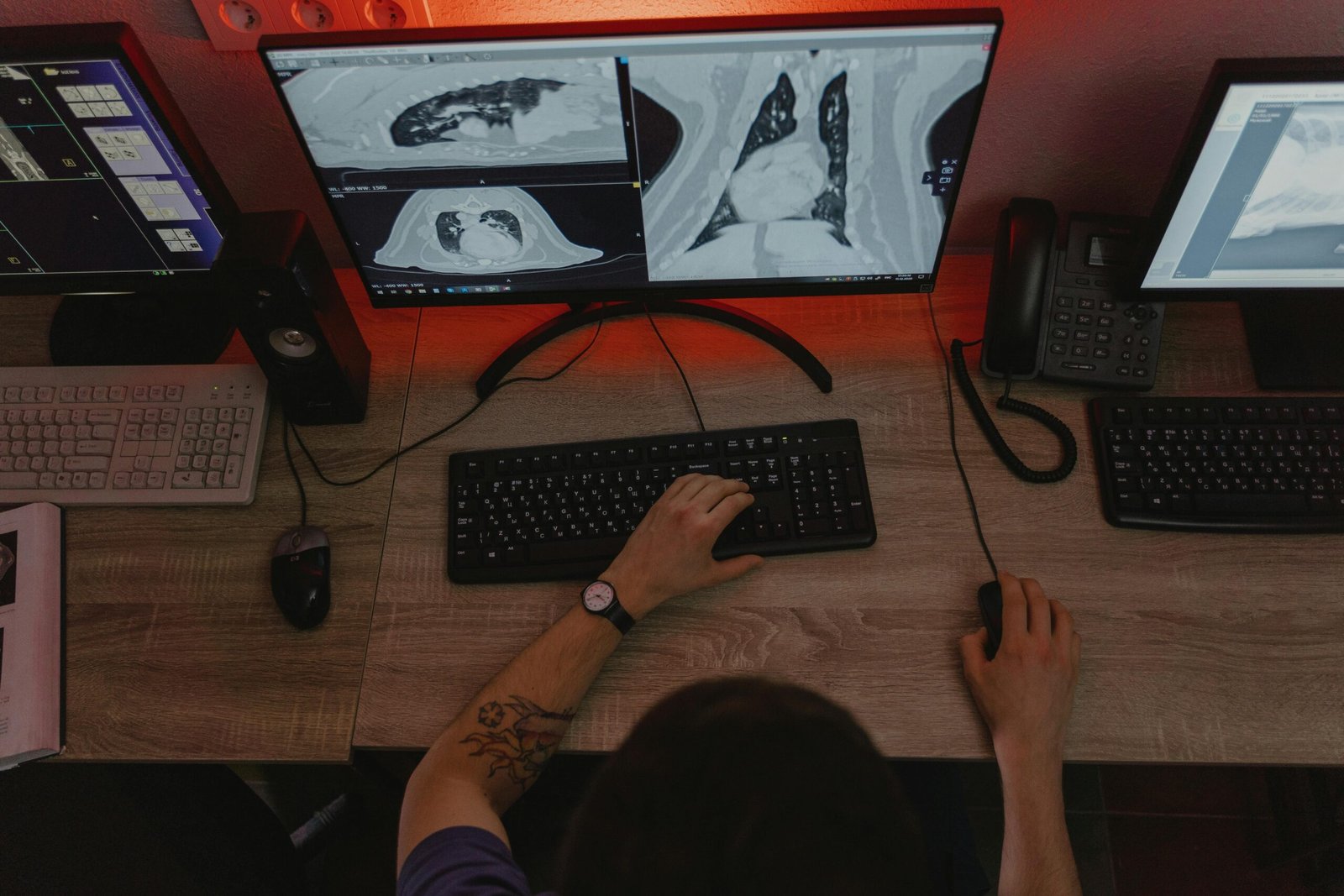 A radiologist reviews x-ray scans on multiple monitors at a desk, focusing on medical diagnostics.